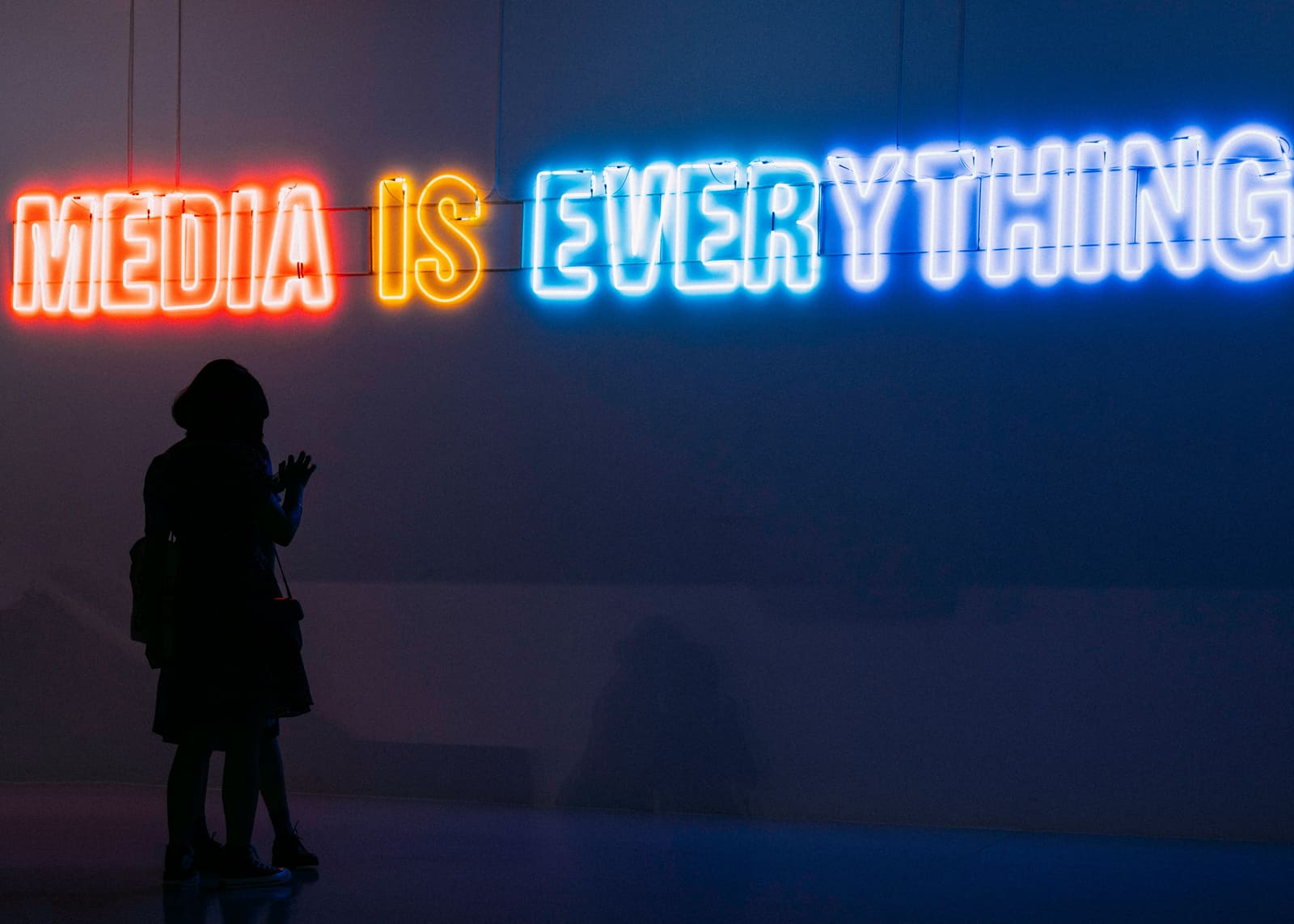 Illuminated neon sign reading "Media is everything" on a gallery wall